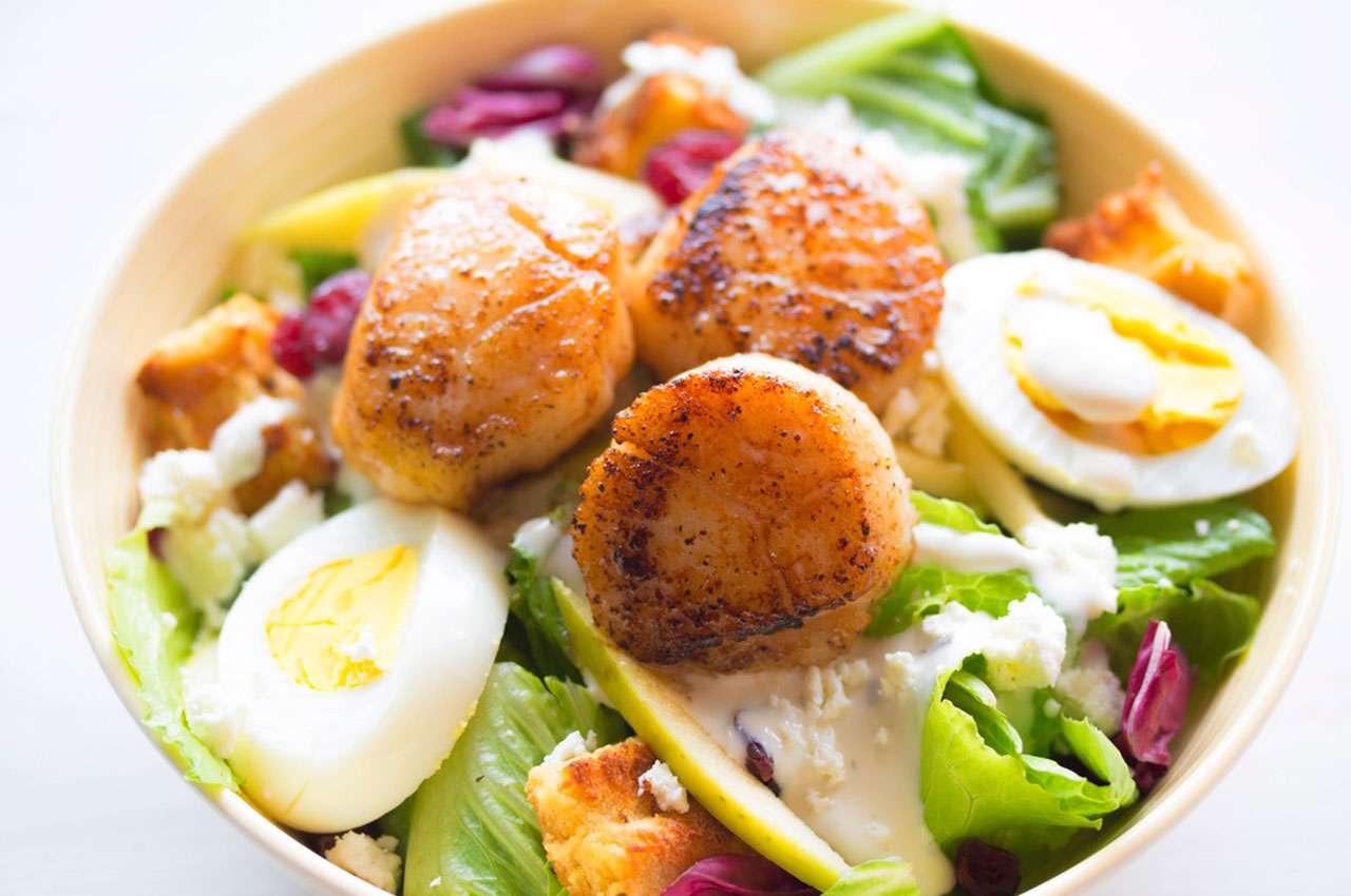 Perfectly seared scallops with boiled eggs on a bed of fresh greens